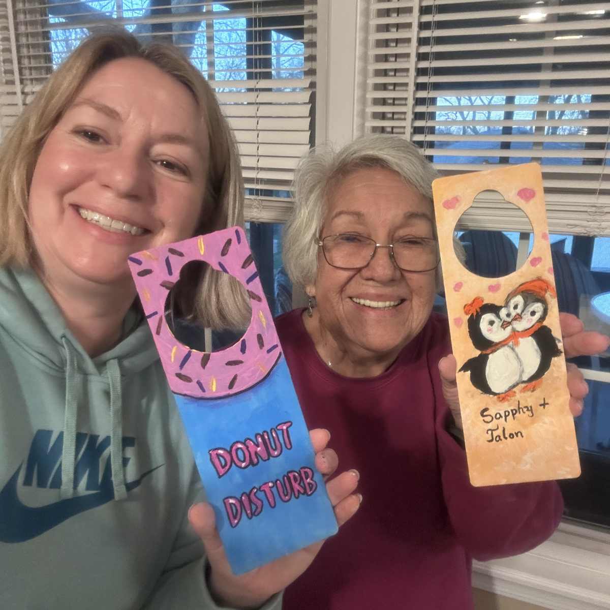 Mother and grandmother holding finished painted wooden door hangers made with UnchainedBrainz party craft kit