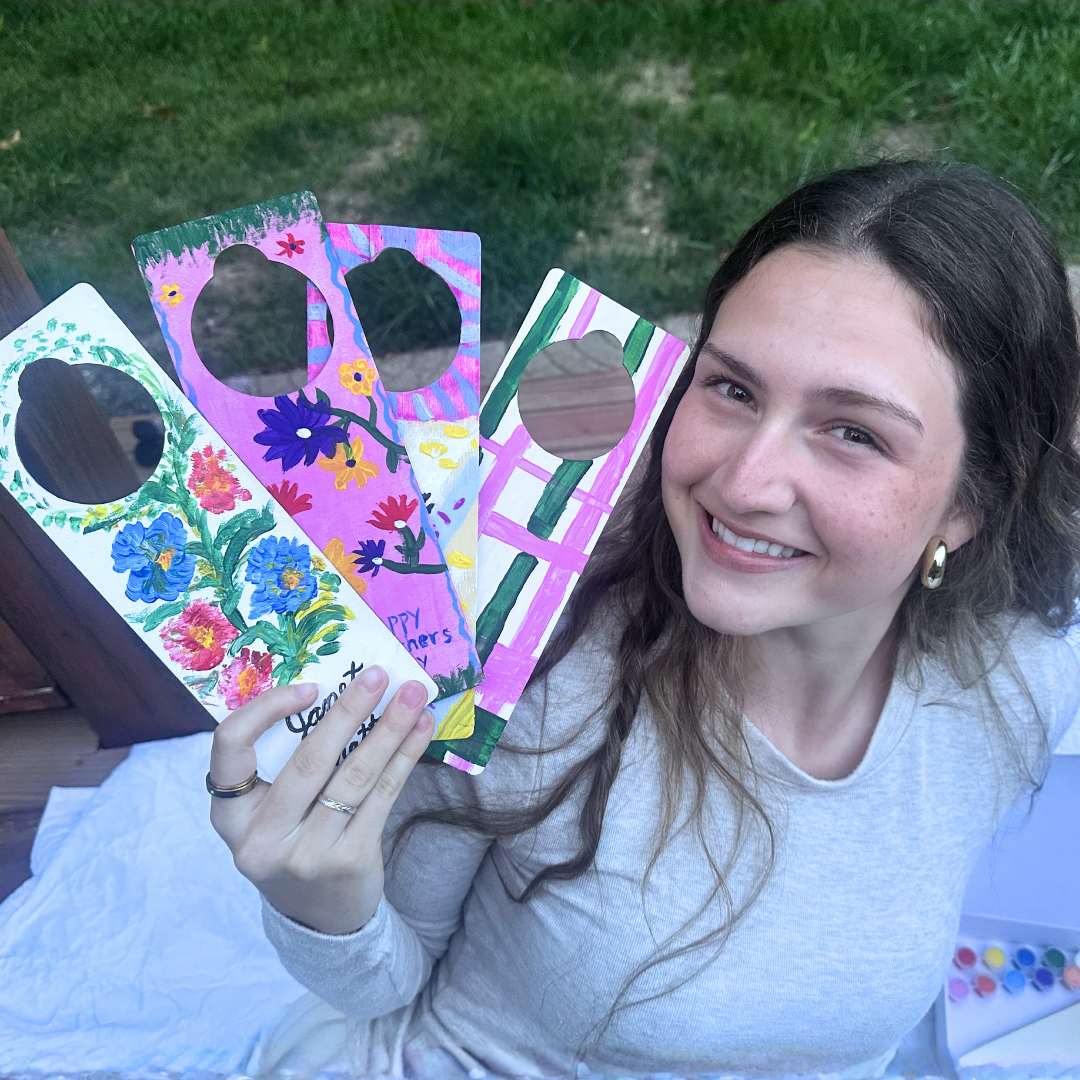 Girl holding colorful painted diy doorhangers as a gift created with friends outdoors as a screen free picnic activity