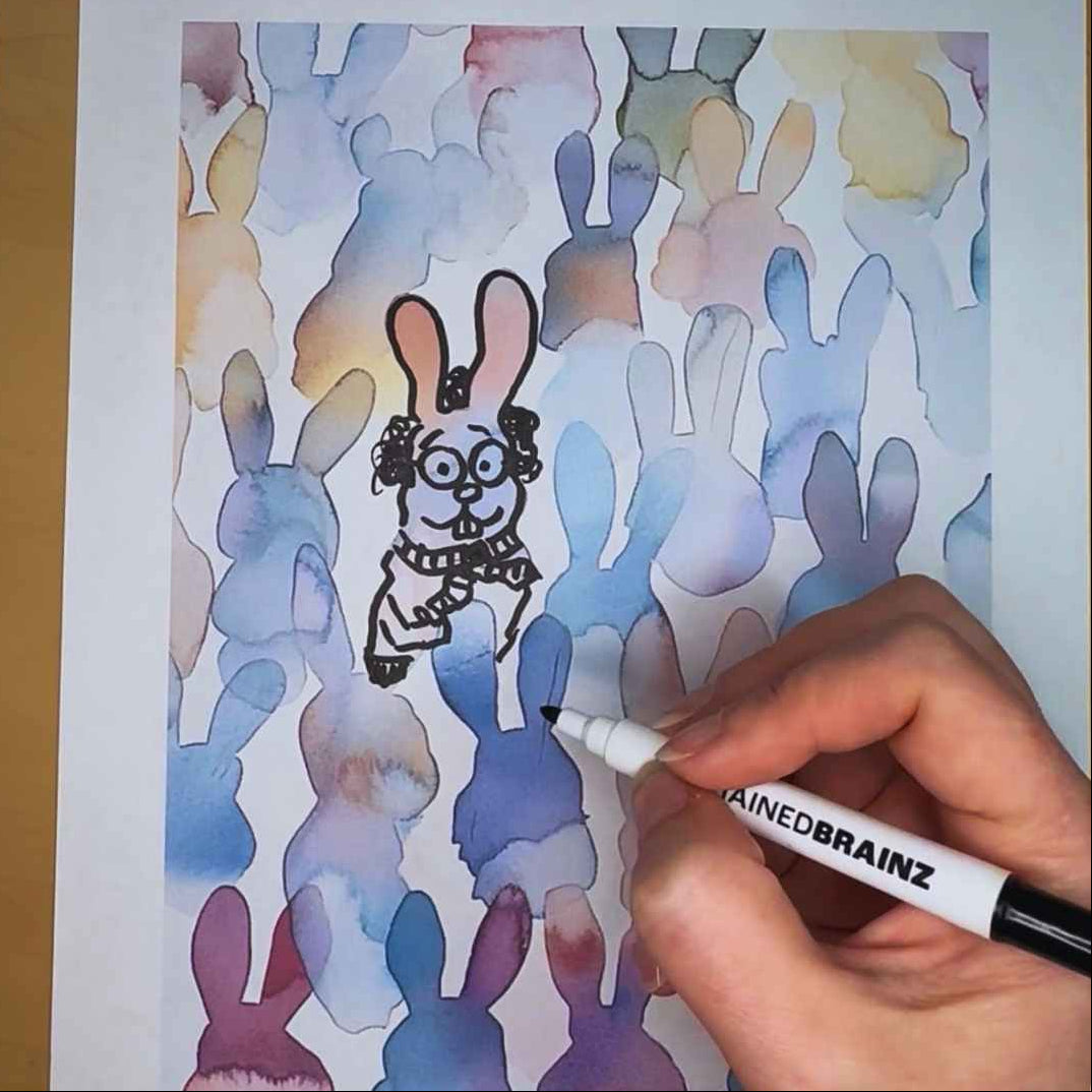 Hand holding a marker over a drawing of a cartoon character with watercolor bunny outlines.