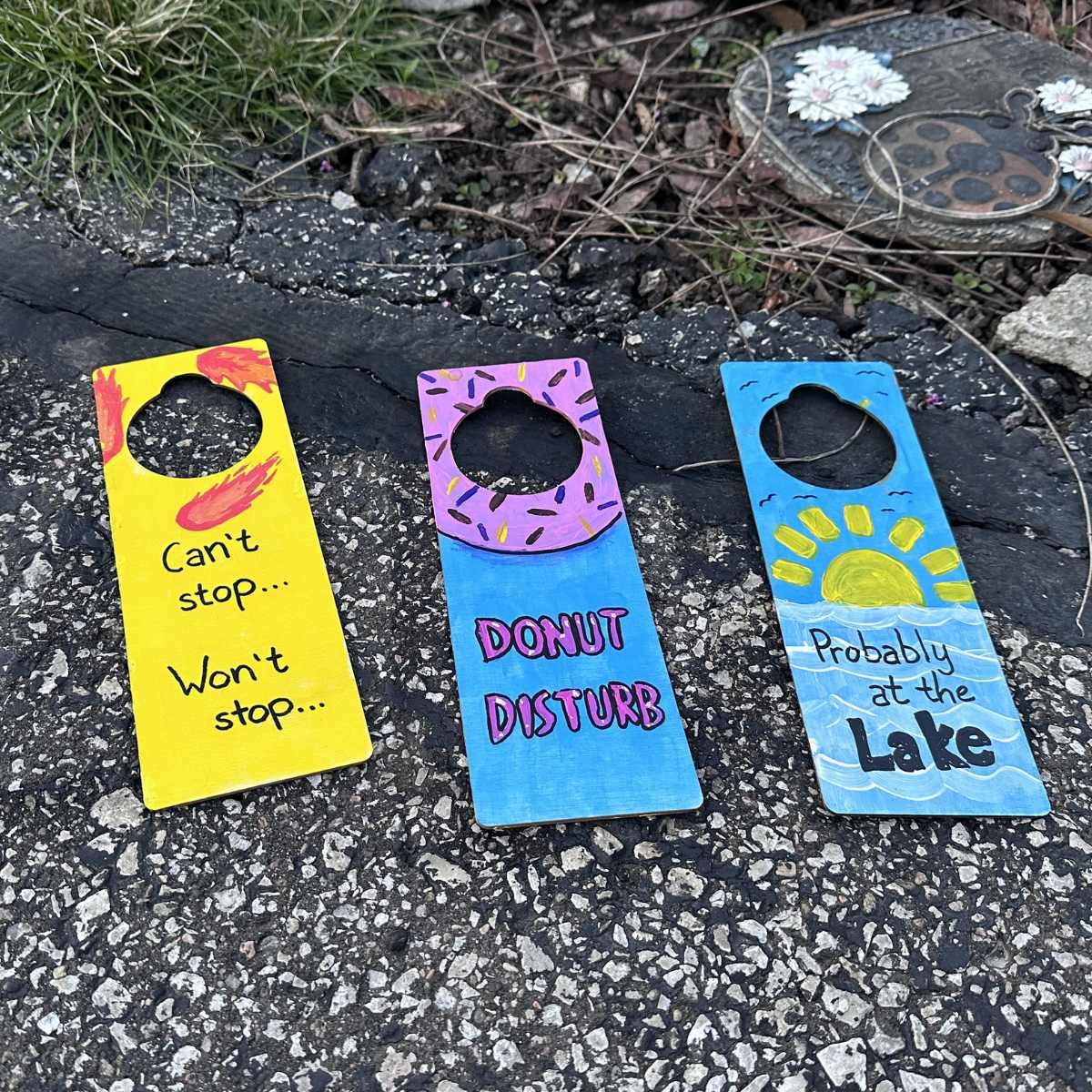 Three colorful door hangers with humorous text on a textured surface.