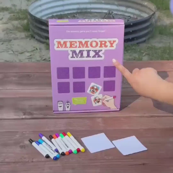 A purple "Memory Mix" game box on an outdoor wooden table. A person draws matching pictures, a fish, flag, soccer ball, bike, and sun, on blank cards, flips them face-down into a grid, then turns over two matching cards to find a pair.